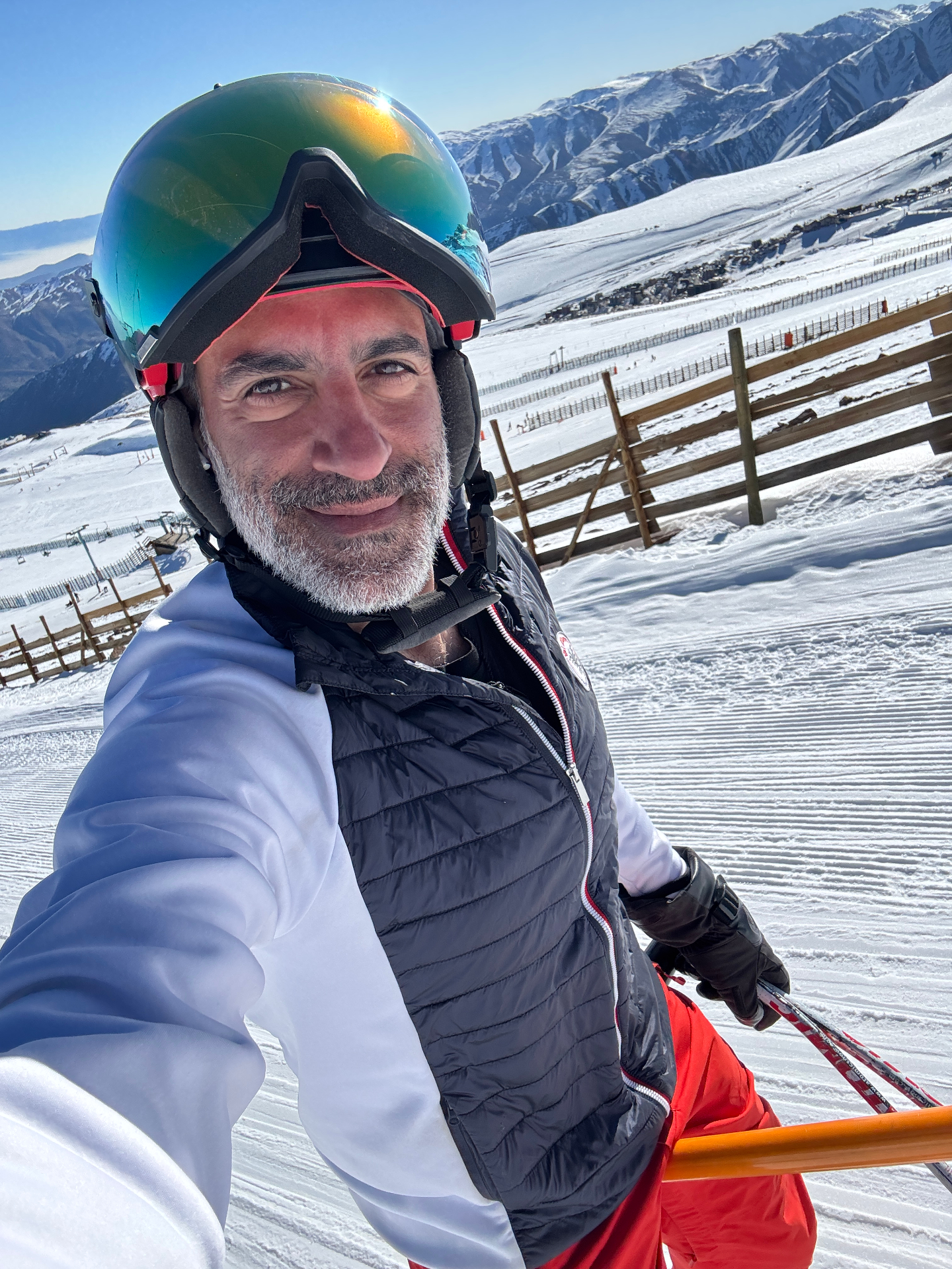 Cogo on skis in the mountains, wearing a helmet and ski gear with snowy peaks behind him